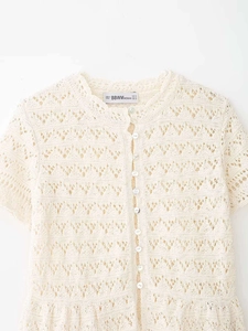 Close-up of cream knit cardigan featuring delicate crochet patterns and pearl buttons