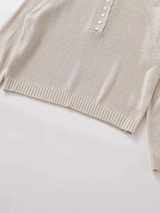 Detail view of rib-knit cuffs and Henley neckline with five white buttons on beige sweater