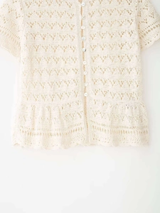 Detail of crochet hollow-out knit cardigan with round buttons and ruffle hem