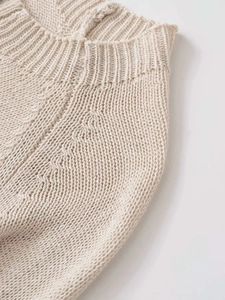 Close-up of beige knit sweater showing ribbed crew neck and cable knit texture details