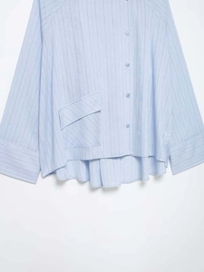 Detail view of light blue striped shirt featuring a unique asymmetric pocket and hem