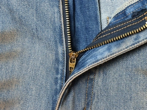 Detailed macro shot of high-quality metal YTV zipper on blue distressed denim jeans