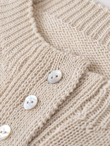 Close-up of beige knit cardigan with textured ribbing and pearl buttons detail