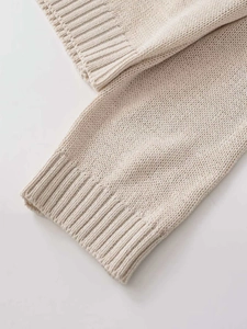 Close-up detail of beige knit sweater showing ribbed cuffs and fine stitch texture