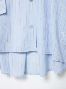 Detail of light blue striped shirt hem featuring asymmetrical cut and side patch pocket