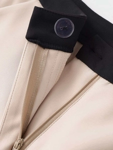 Détail macro du tissu sergé, taille contrastée et braguette zippée sur le pantalon beige