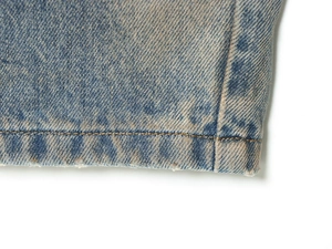 Detailed macro view of light blue denim fabric with yellow stitching and frayed hem