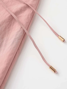 Detail of pink fabric drawstring waist with polished gold metal ends on casual pants