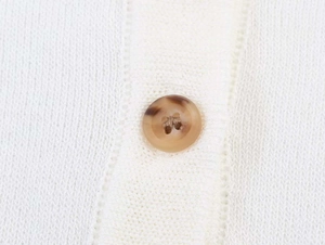 Detail of white knit fabric texture featuring a brown tortoiseshell patterned button