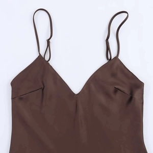 Détail d'un caraco en satin marron foncé avec col en V, fines bretelles et texture lisse
