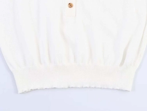 Close-up of white knit top featuring wooden button detail and ribbed hem texture