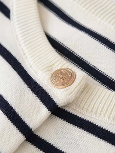 Close-up of a vintage gold crest button on a navy and beige striped knit cardigan