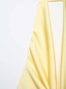 Detailed view of pale yellow satin dress fabric with a glossy finish and fluid drape
