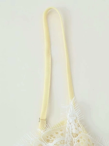 Detailed close-up of yellow camisole dress featuring white eyelash lace trim and strap