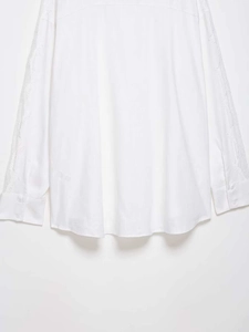 Detailed view of delicate lace embroidery on long sleeves of a white cotton blouse