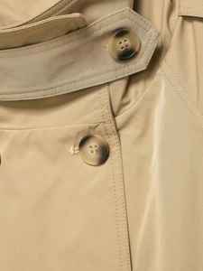 Detail of khaki trench coat featuring tortoise shell buttons and premium fabric texture