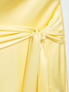 Close-up of light yellow satin dress featuring cross knot and pleated waist details