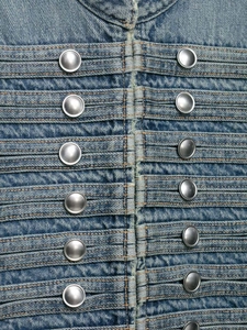 Vista de detalle de mezclilla azul vintage con pliegues y botones metálicos plateados