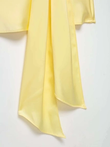 Detail of the light yellow satin dress showing soft fabric texture and ribbon tie design