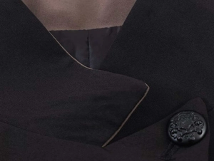 Close-up of black blazer lapel detail and textured vintage button on woven fabric
