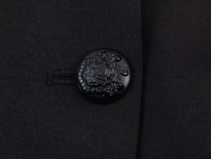 Detailed macro shot of an embossed black crest button on a blazer's textured fabric