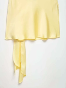 Detail of light yellow satin dress showing smooth fabric texture and drape tie element