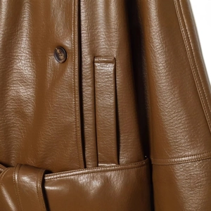 Détail d'une veste en cuir marron foncé montrant le bouton, les coutures et la texture