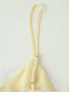 Detail of adjustable straps and white eyelash lace on a silky yellow satin slip dress