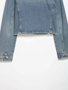 Detalle del dobladillo deshilachado y botones metálicos en una chaqueta vaquera azul