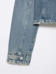 Detalle de la manga de chaqueta vaquera azul claro con botón metálico y dobladillo deshilachado