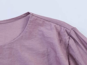 Detail von Rundhalsausschnitt und Rüschennaht an staubrosa Bluse mit Faltenstruktur