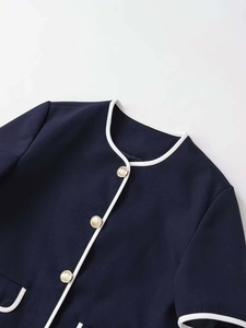 Detail of navy blue knit jacket featuring white contrast piping and embossed gold buttons