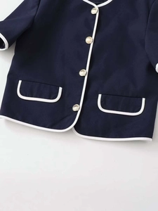 Detail of navy blue cardigan featuring white contrast piping and gold metal buttons