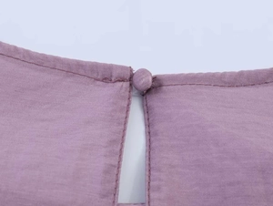 Detailansicht aus mauvefarbenem Rüschenstoff mit stoffbezogenem Knopf und präziser Naht