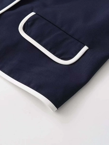 Detail of navy blue cardigan showing patch pocket and white piping on woven fabric
