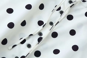 Detail of black polka dot fabric on white blouse with round buttons and fabric texture