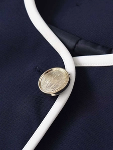 Close-up of navy knit cardigan with white trim and textured gold metallic button