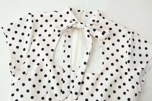 Détail du chemisier à pois avec nœud de cravate et découpe goutte sur tissu blanc