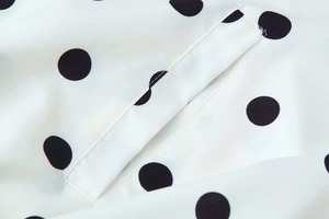 Close-up of high-quality stitching and black polka dots on white chiffon fabric jacket