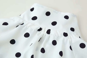 Detailed view of white high-neck blouse featuring large black polka dots and fine fabric texture