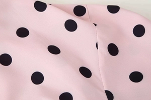 Close-up of light pink fabric with large black polka dots and fine stitching detail
