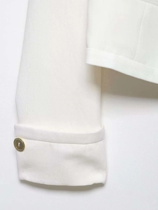 Close-up of white tweed jacket with textured fabric and elegant gold metal button detail
