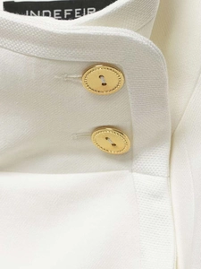 Macro detail of white blazer fabric with elegant golden sunburst metal buttons