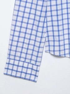 Détail de la chemise à carreaux bleu et blanc montrant le poignet et l'ourlet cousu