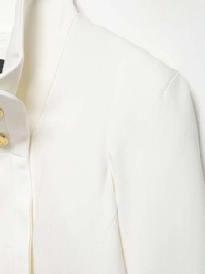 Detailed close-up of white cropped blazer fabric and textured golden metal button