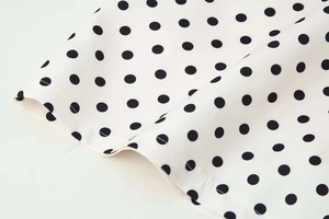Détail d'un tissu léger blanc à pois noirs montrant une texture tissée et fluide
