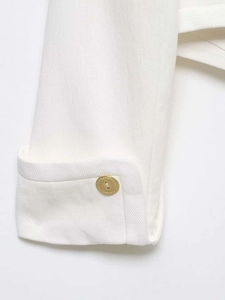 Detail of sleeve cuff on white cropped blazer featuring a textured gold metal button