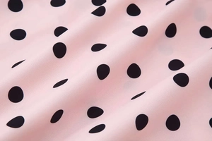 Detailed macro view of soft pink chiffon fabric with classic black polka dots and draped folds