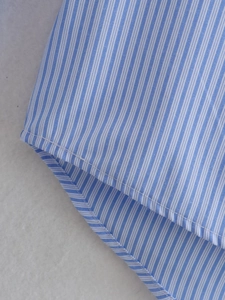 Detailed macro view of the curved hem and fine blue and white vertical stripes fabric