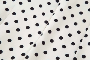 Détail du tissu blanc à pois noirs vintage sur une robe à la texture lisse et fluide